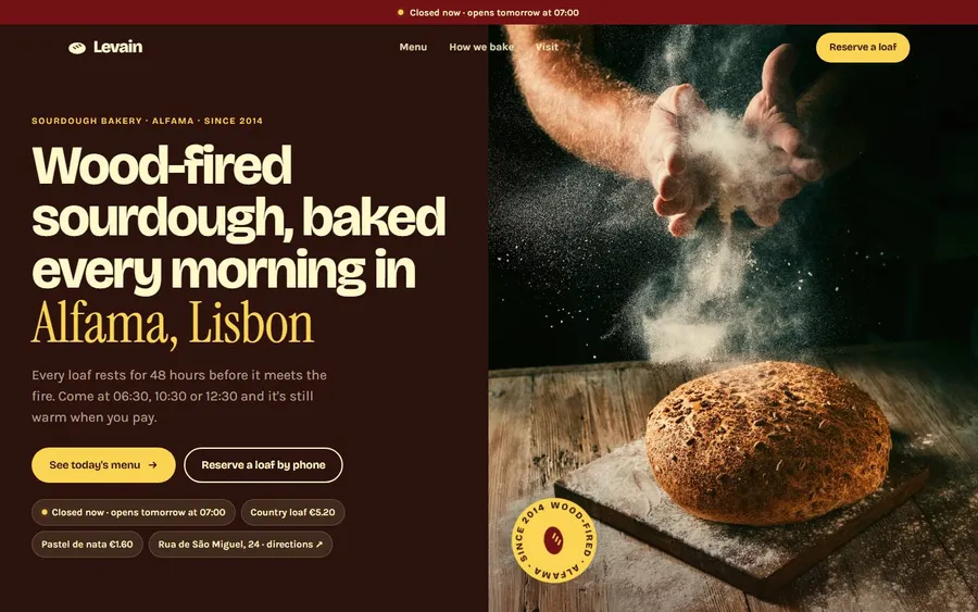 Levain bakery homepage — dark rosewood hero, bold headline, hands dusting flour over a sourdough loaf